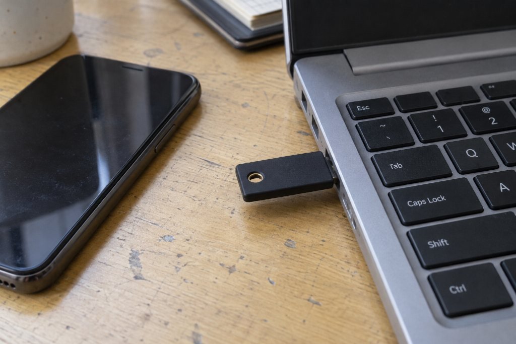 A USB drive plugged into a laptop on a wooden desk, a phone and notebook nearby