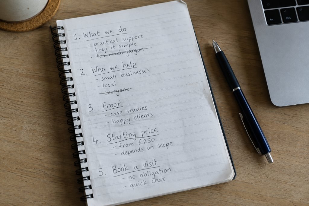 An open spiral notebook with a handwritten five-point list: what we do, who we help, proof, starting price, book a visit